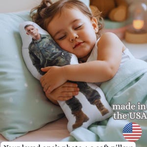 May include: A sleeping child cuddles a custom pillow featuring a photo of a person in military uniform. The pillow is white with a full-body image. The text reads "Your loved one's photo + a soft pillow = hugs even when they're far away."