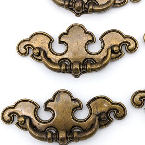 May include: Set of four antique gold cabinet drawer pulls with a decorative, ornate design. Each pull features a curved handle with a rounded knob on each end.