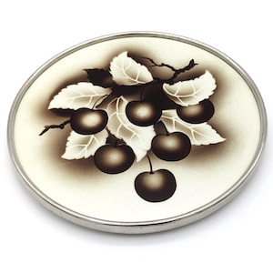 May include: A white ceramic coaster with a silver rim features a black and white illustration of cherries on a branch with leaves.