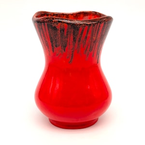 Pode incluir: Um vaso de cerâmica vermelho vibrante com um acabamento brilhante. O vaso tem um corpo bulboso e uma borda ondulada e alargada. Gotas marrons escuras descem da borda, criando um contraste marcante. Um item decorativo.