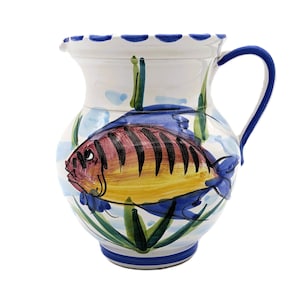 Könnte beinhalten: Eine weiße Keramikkanne mit blauem Henkel und einem handbemalten Design eines gelben, roten und blauen Fisches mit grünen Algen.
