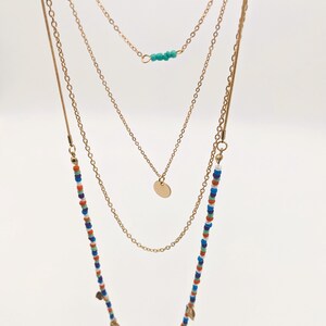 May include: A gold layered necklace with a charm pendant, turquoise beads, and a beaded strand with gold leaf accents.