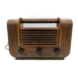 May include: A vintage wooden radio with a brown wood cabinet and a metal grille. The radio has a dial with numbers and letters, and three knobs on the front.
