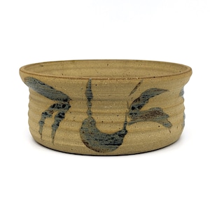May include: A tan ceramic bowl with a blue and brown floral design. The bowl has a rounded shape and a slightly flared rim.