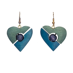 Puede incluir: Un par de pendientes en forma de corazón. Cada pendiente está dividido diagonalmente en dos secciones, una verde y otra azul. Una esfera de color púrpura oscuro está colocada en el centro de cada pendiente. Los pendientes cuelgan de ganchos dorados.