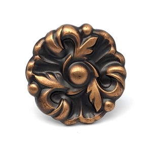 May include: A round, ornate, copper-toned cabinet knob with a black background and intricate floral designs.