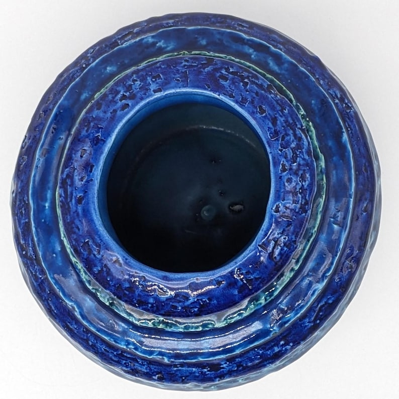 Op de afbeelding: Een blauwe keramische vaas met een getextureerd, gelaagd ontwerp. De vaas heeft een brede opening en een ronde vorm.