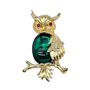 Peut inclure: Broche en forme de hibou doré avec des yeux en strass rouges et un grand centre ovale vert émeraude. Le hibou est perché sur une branche dorée. Bijou de style vintage.