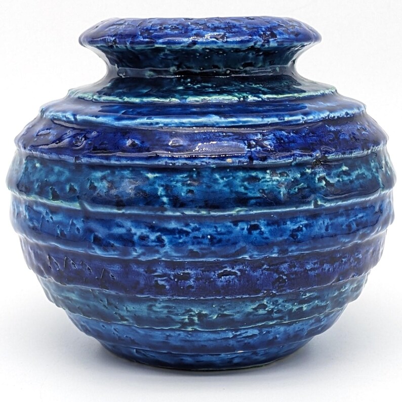 Op de afbeelding: Een blauwe en groene keramische vaas met een ronde vorm en een getextureerd oppervlak. De vaas heeft een brede opening en een smalle hals.