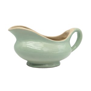 May include: A light green ceramic gravy boat with a handle. The boat has a smooth, glossy finish.