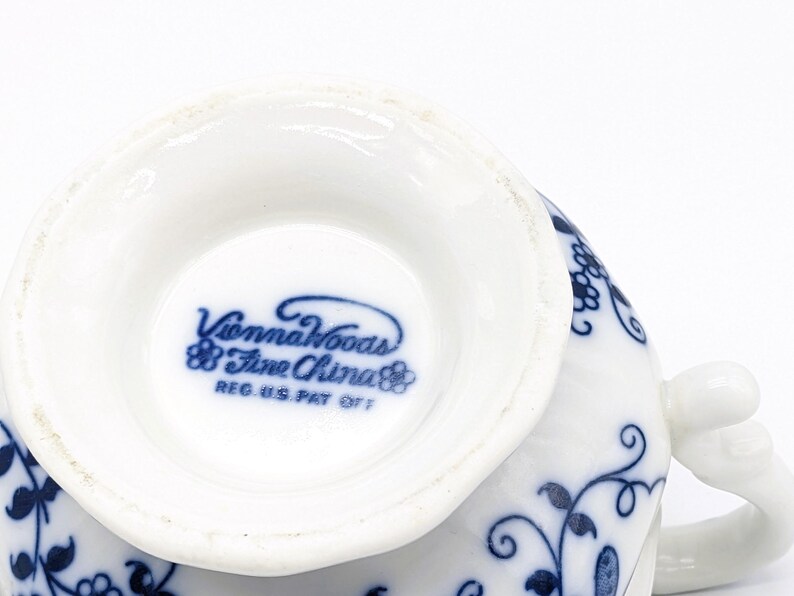 Pu&ograve; includere: Primo piano del fondo di una tazza da t&egrave; bianca con un motivo floreale blu. L'iscrizione "Vienna Woods Fine China" &egrave; stampata in blu sul fondo della tazza.