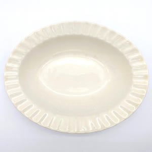 May include: Cream-coloured oval serving dish with a ruffled edge. The dish has a smooth, glossy surface and a shallow depth. The ruffled edge adds a decorative touch. Suitable for serving appetizers or side dishes.