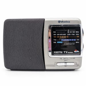 May include: A Vextra brand portable radio with a dark gray fabric speaker grille on the left and a silver plastic body on the right. The display panel features AM, FM, TV1, TV2, and weather band frequencies with white text and a small sun icon.