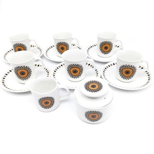 May include: A set of six white teacups and saucers with a black and orange floral design. The set also includes a sugar bowl and creamer.