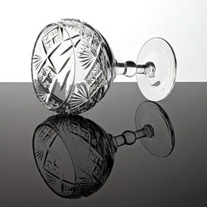 Puede incluir: Una copa de vidrio transparente con un diseño de cristal tallado. La copa tiene una copa ancha y un tallo largo con una base redonda.