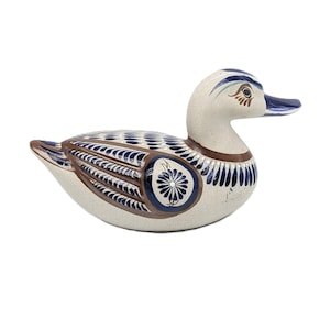 May include: Hand-painted ceramic duck figurine with blue and brown accents. The duck has a white body with blue and brown floral designs.