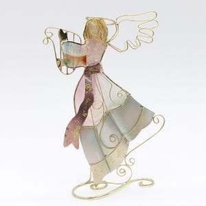 May include: A decorative angel figurine made of gold-coloured wire and stained glass. The angel is playing a harp and has wings. The dress is a mix of pastel colours, including pink, blue, and gold accents. The figurine stands on a decorative base.