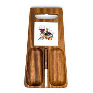 Puede incluir: Tabla de servir de madera con asa y dos secciones empotradas. Una baldosa cuadrada en el centro presenta una copa de vino, uvas y pescado. Se incluye un cuchillo pequeño. La tabla es de madera de tono cálido.