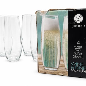 May include: A set of four clear glass flutes standing next to their original packaging box. The box features the Libbey logo, the text 4 GLASSES, 9.7oz, and WINE & DINE PREMIUM. The glasses have a curved, stemless design with a narrow base and rim.