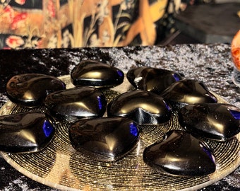 May include: A collection of black heart-shaped stones on a gold and black circular plate. The stones have a shiny, polished finish.