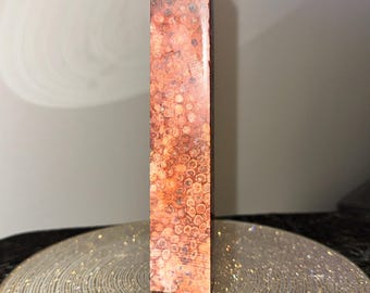 May include: A tall, pointed, red and brown crystal with a unique pattern. The crystal is standing on a round, sparkly, gold-colored surface.