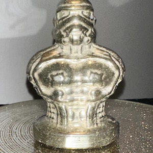 May include: A silver-colored ceramic figurine of a Star Wars Stormtrooper. The figurine is detailed with a textured surface and has a round base.