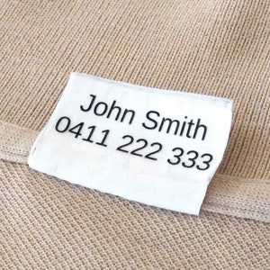 May include: White fabric label with black text that reads "John Smith 0411 222 333".