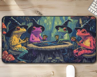 May include: A rectangular mousepad featuring a whimsical illustration of four colorful frogs wearing witch hats, gathered around a table. The frogs are playing cards in a forest setting with mushrooms and trees. The mousepad has a dark blue background.