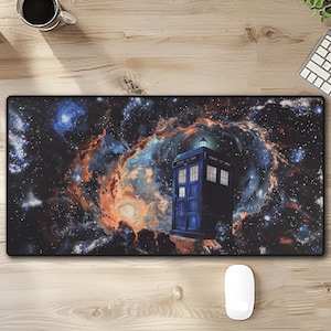 May include: A rectangular mouse mat featuring a blue police box against a backdrop of a colourful nebula and stars. The mat is on a wooden desk with a computer, keyboard, and a cup of coffee.