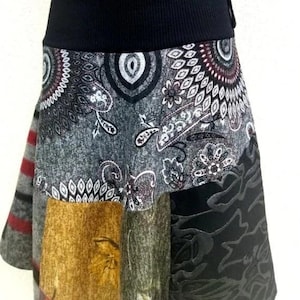 Könnte beinhalten: Ein Patchwork-Rock mit einem schwarzen Bund. Der Rock besteht aus verschiedenen Stoffen mit verschiedenen Mustern, darunter Paisley, Blumen und geometrische Muster. Die Farben sind Grau, Schwarz, Braun und Rot.