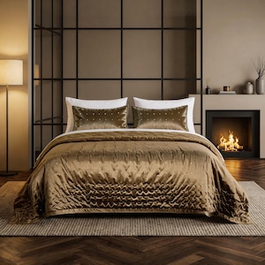 May include: A bed featuring a metallic bronze velvet quilt with a quilted texture and small stud embellishments. Two matching rectangular bronze velvet pillows with stud details are placed in front of two plain white rectangular pillows.