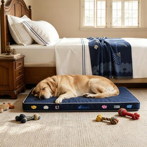 May include: A golden retriever sleeping on a rectangular navy blue dog bed with white piping. The bed features the text Netbors and several small colorful patches along the front edge. Several rope dog toys are scattered on the floor.