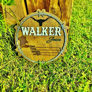 May include: A wooden sign with a barbed wire border and a silhouette of a longhorn steer. The sign says "WALKER James" and has spaces to fill in the date, time, weight, and length.