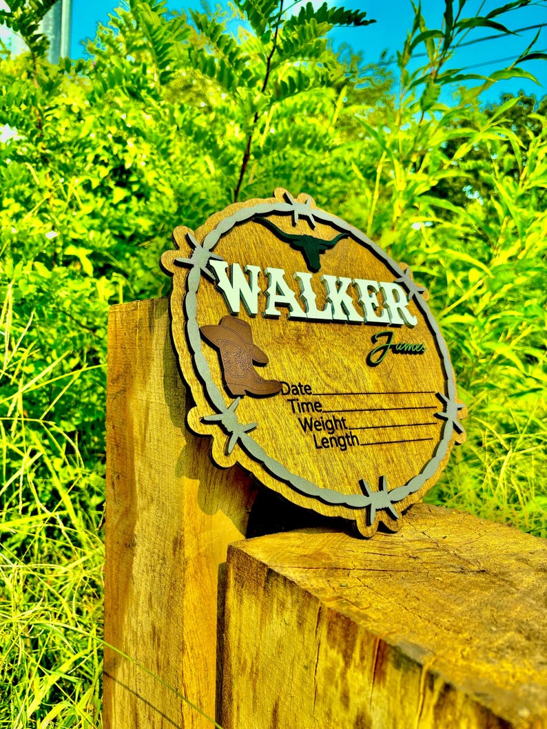 May include: A wooden sign with a rustic design featuring a barbed wire border and a silhouette of a longhorn steer. The sign is personalized with the name "WALKER" and includes spaces to record the date, time, weight, and length.