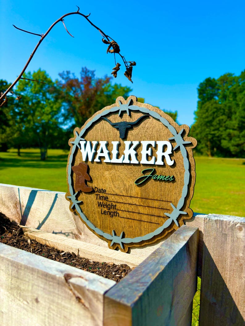 May include: A wooden sign with a rustic brown finish and a blue and green barbed wire design. The sign says "WALKER James" and has spaces to fill in the date, time, weight, and length.