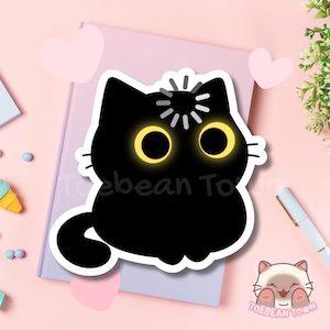 Può includere: Un adesivo a forma di gatto nero con grandi occhi gialli e un contorno bianco. Il gatto ha una piccola esplosione bianca sopra la testa. L'adesivo è su un quaderno viola chiaro con cuori rosa e il testo "Toebean Town".
