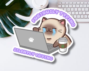 May include: A sticker featuring a cartoon cat with a laptop and a cup of coffee. The cat is crying and the text says "Furiously Typing Silently Crying".