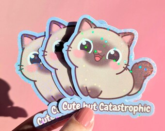 May include: Three stickers featuring a cartoon cat with a light brown coat, pink cheeks, and a blue outline. The cat has a happy expression with its tongue sticking out. The text "Cute but Catastrophic" is below the cat.