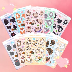 May include: A selection of sticker sheets with cat illustrations. Each sheet displays different cat breeds and poses, with the text "TOEBEAN DIARIES" at the top. The stickers are set against a pink background with decorative elements.