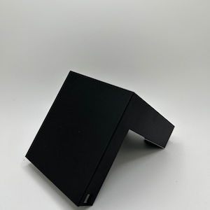 Może przedstawiać: Czarny plastikowy wspornik narożny do półki. Wspornik jest przeznaczony do montażu na ścianie i ma płaską powierzchnię do trzymania przedmiotów.