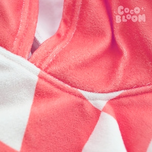 Peut inclure: Gros plan sur un tissu ray&eacute; rose et blanc avec un d&eacute;tail de couture. Le tissu est doux et moelleux, avec une texture velout&eacute;e.
