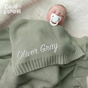 May include: A soft, sage green knitted baby blanket with the name "Oliver Gray" embroidered in white.