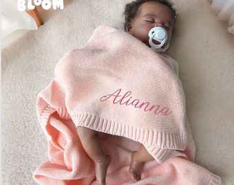 May include: A pink knitted baby blanket with the name "Alianna" embroidered on it. The blanket is draped over a baby doll.