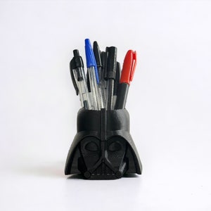 May include: A black Darth Vader-shaped desk organiser with a variety of pens and markers inside.