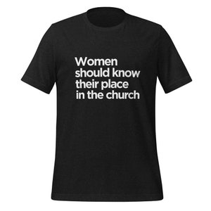 May include: Black t-shirt with white text that reads "Women should know their place in the church."