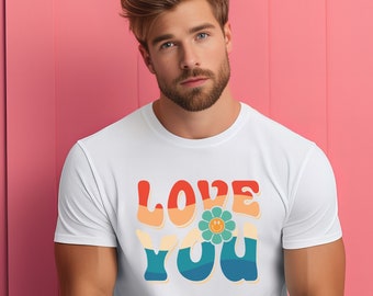 Può includere: Una maglietta bianca con un design grafico retrò che dice "LOVE YOU" in lettere colorate con un fiore sorridente al centro.