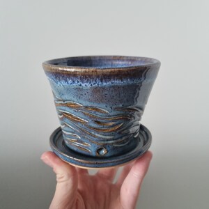 May include: A blue and brown ceramic planter with a wavy design. The planter has a drainage hole and a matching saucer.