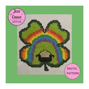 Puede incluir: Patrón de punto de cruz de un trébol de cuatro hojas verde con un arcoíris arqueado sobre él. Se puede ver la cara de un duende debajo del arcoíris. El patrón está etiquetado como "PATRÓN DIGITAL".