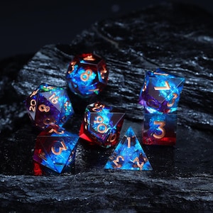 Puede incluir: Juego de siete dados poliédricos con un diseño celestial. Los dados son transparentes con un patrón azul y rojo similar a una galaxia y numeración dorada. Los dados están dispuestos sobre una superficie oscura y texturizada.
