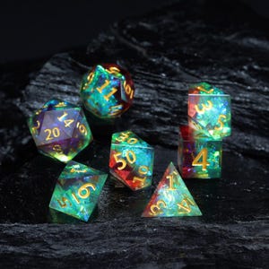 May include: A collection of seven iridescent polyhedral dice with gold numerals. The dice are in various shapes, including a d4, d6, d8, d10, d12, d20, and a d%. The dice have a colourful, gem-like appearance with green, blue, and red tones.